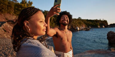 Man and woman on beach and man has mobile phone in hand as example of is sexting cheating