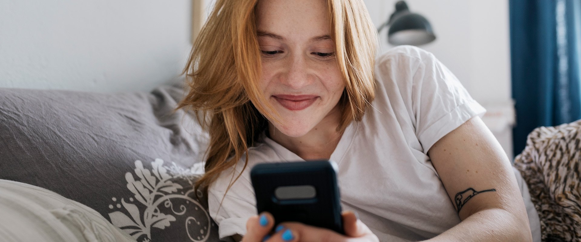 Woman lying in bed and smiling at her mobile phone as a symbol for online dating tips