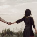 Couple in a field holding hands but walking away from each other