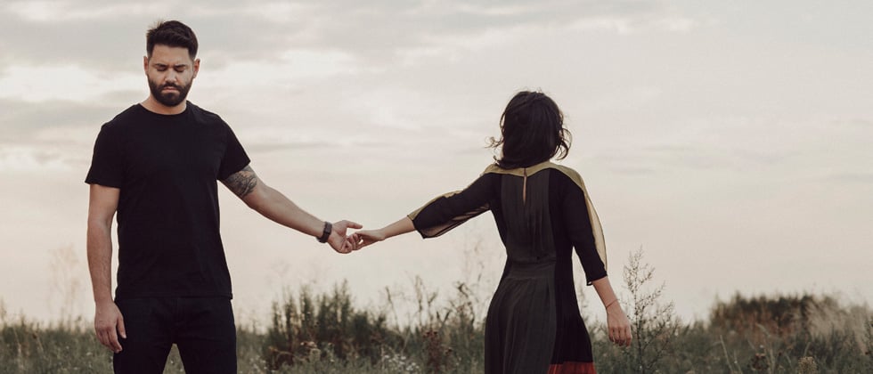 Couple in a field holding hands but walking away from each other