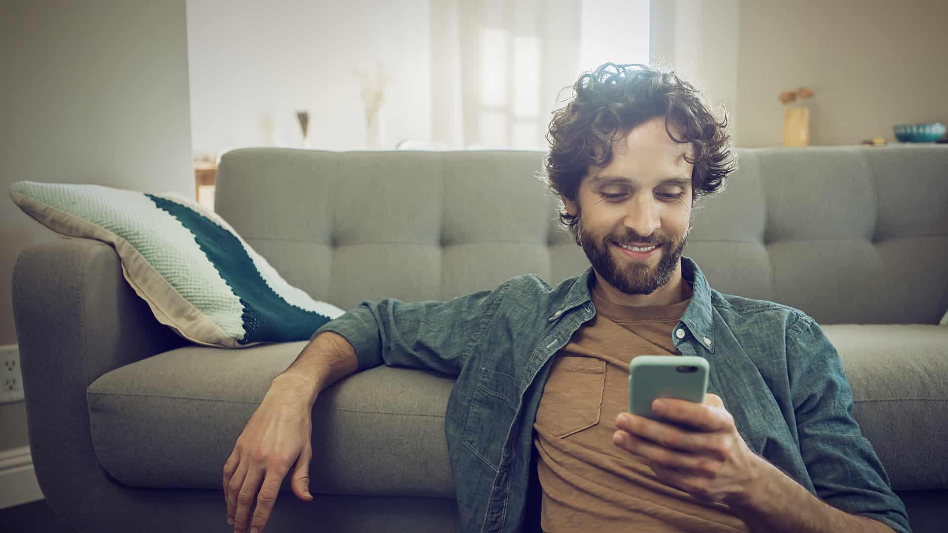 Man sits on the sofa with cell phone and informs himself about eharmony settings