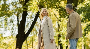 A couple walking through a park next to green trees.