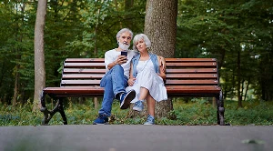 A man is holding a woman's arm as they sit on a park bench.
