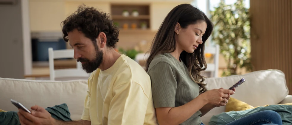 A couple sitting back-to-back, each looking at their phone.