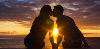Couple kissing at sunset on the beach with the sun between them