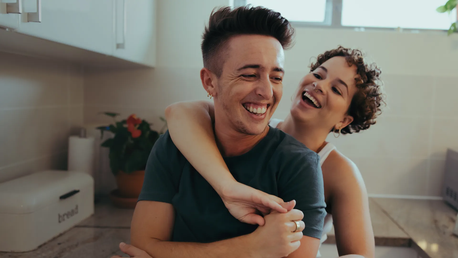 A transgender couple are hugging each other in the kitchen.