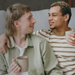 A gay couple are enjoying a cup of coffee together on their sofa.